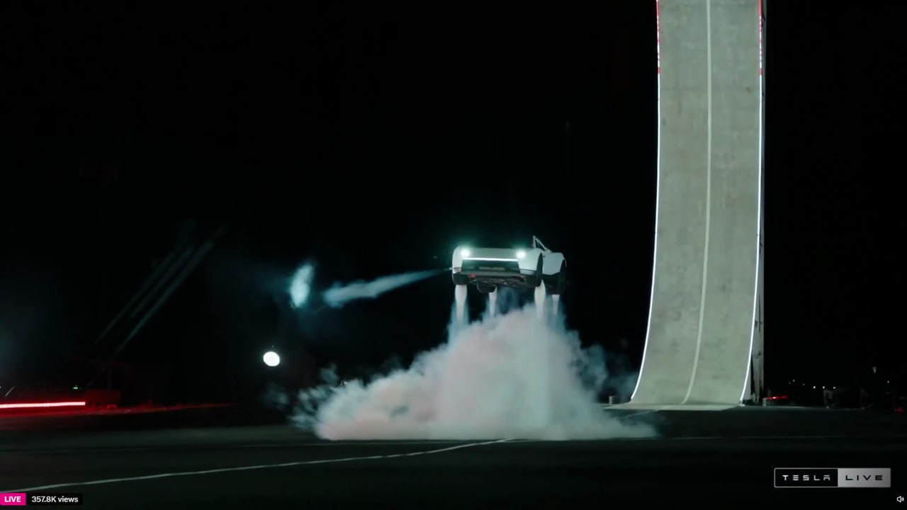 Tesla Roadster suspendido junto a una rampa, con chorros de gas visibles bajo el auto durante la demostración nocturna